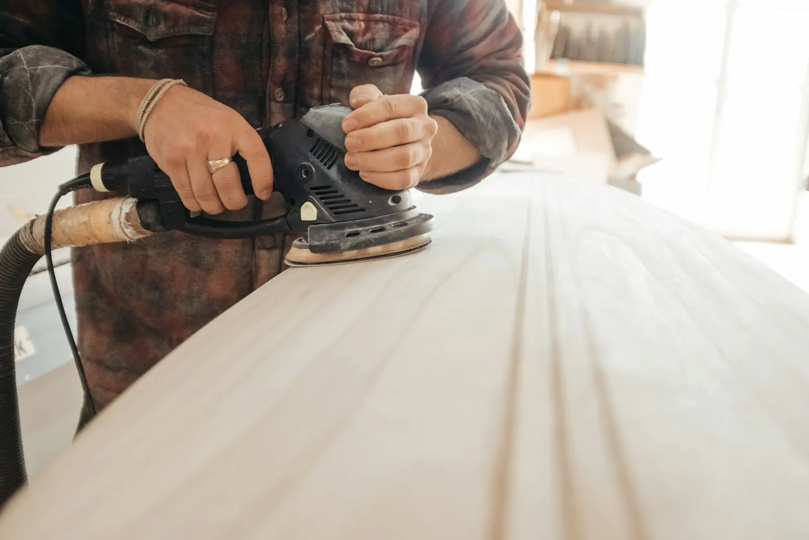 Carpenter sanding a wooden board with a power sander