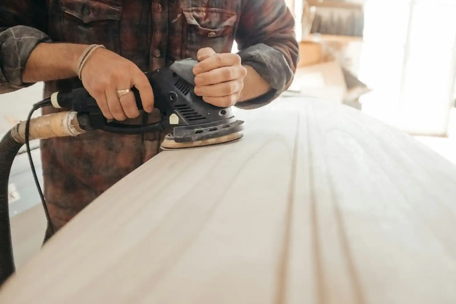 Carpenter sanding a wooden board with a power sander