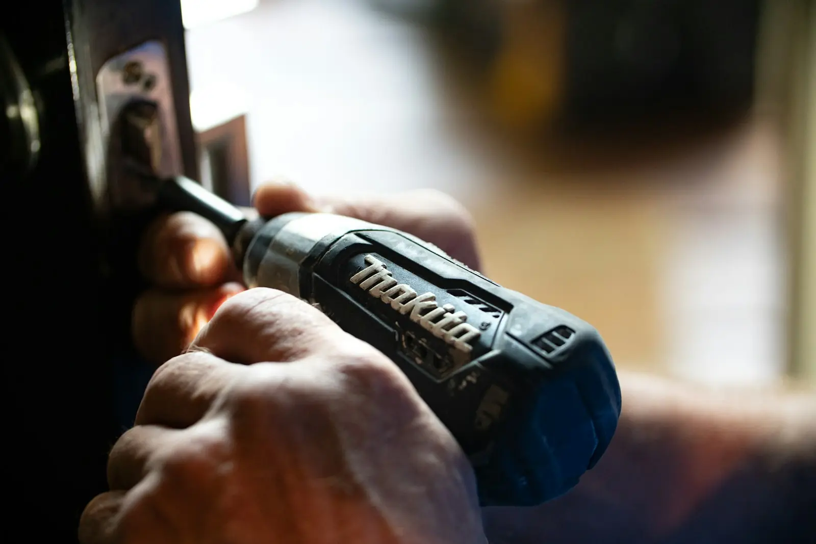 Hand using a cordless drill-driver on a door lock