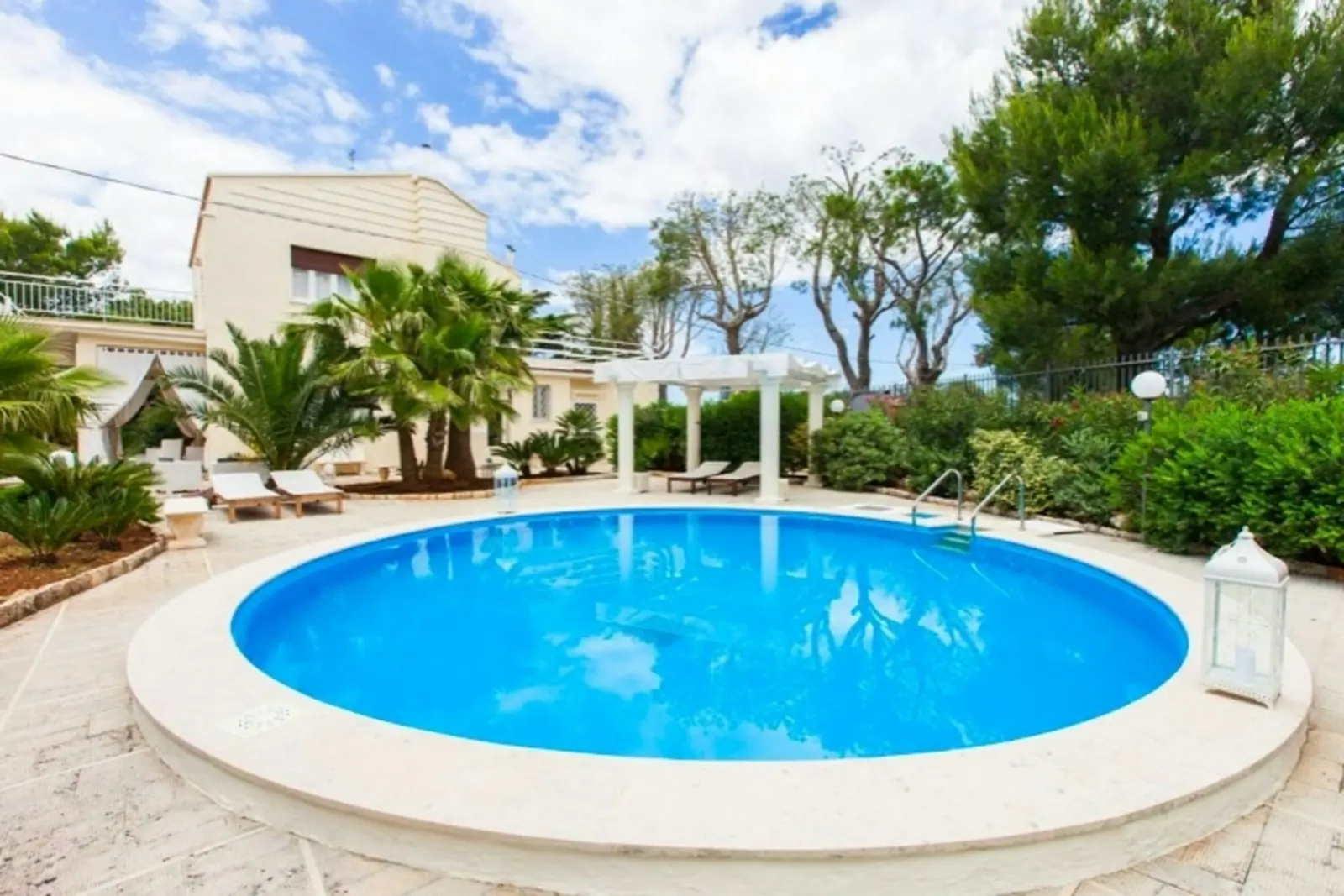 Pergola beside a round swimming pool in a garden with palm trees